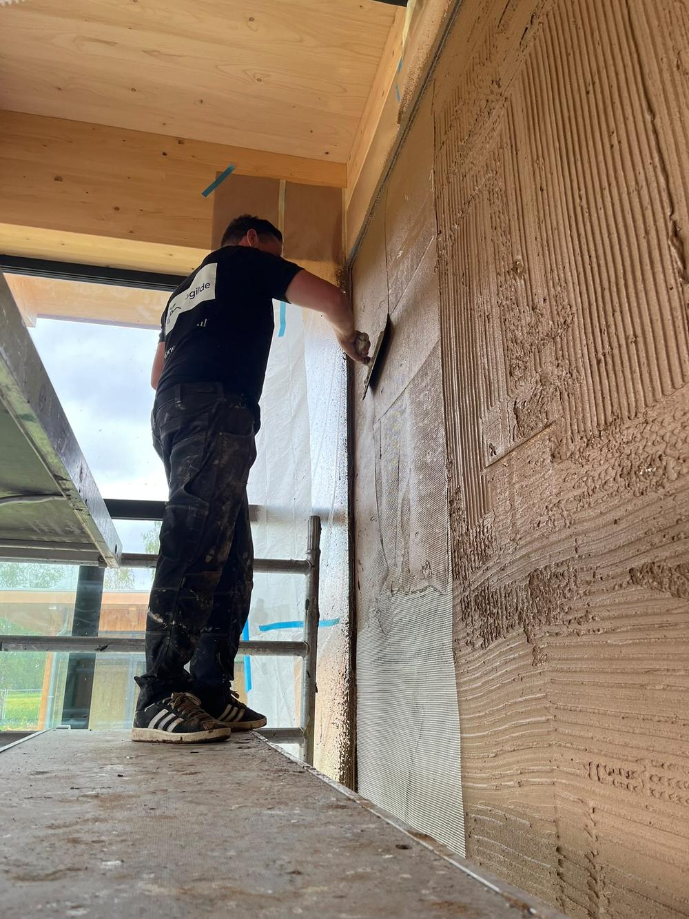 Leemstuc wordt in lagen opgezet op een wand met wapeningsgaas